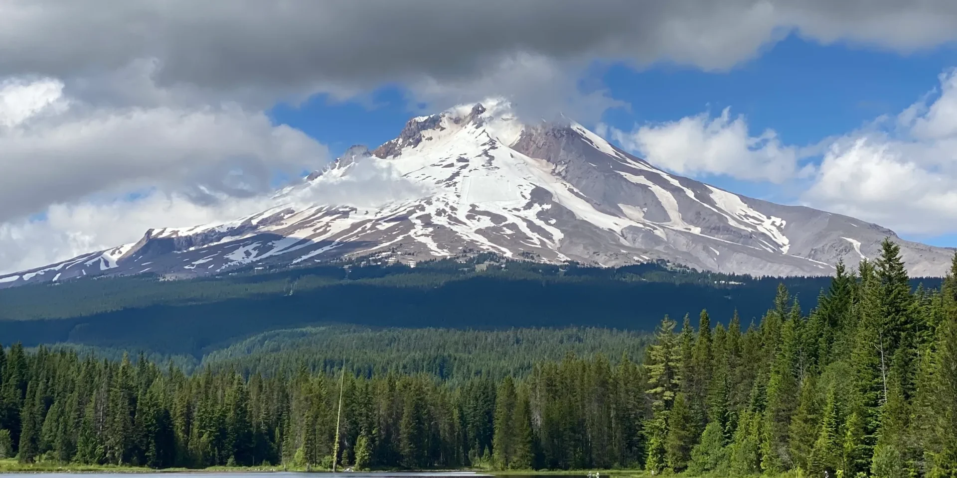 Snow-capped mountain with forest and clouds.