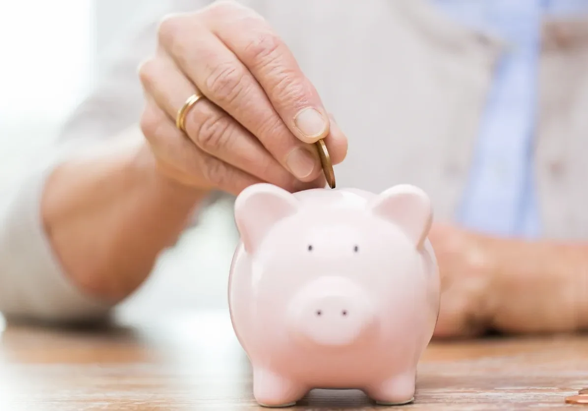 Hand placing coin in pink piggy bank